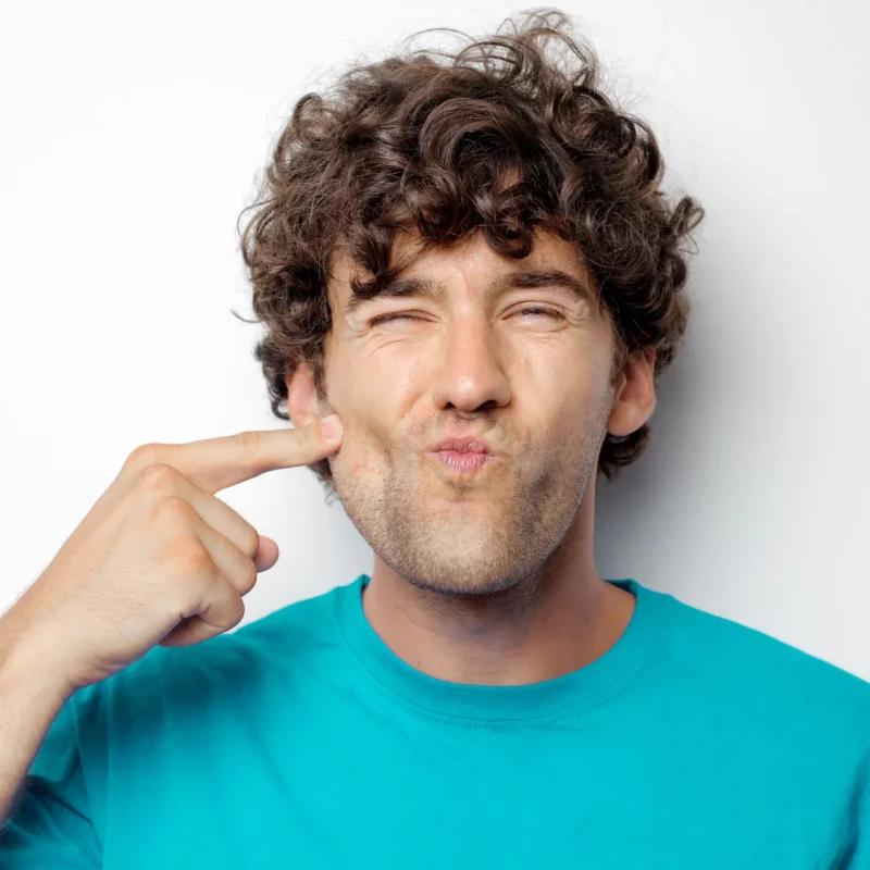 Hombre señalando su mejilla y mandíbula con expresión de incomodidad o dolor muscular facial.